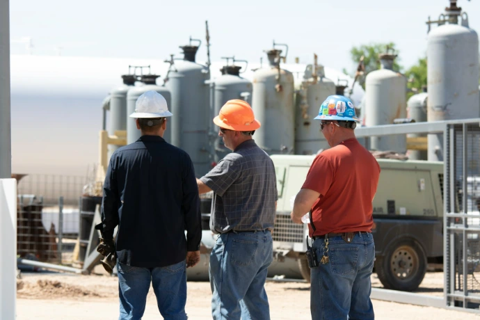 man in black jacket standing beside man in orange shirt in oil and gas industry