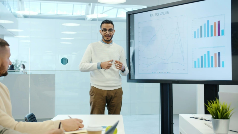 Man presents charts dashboard on a screen during a meeting.